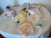 Overview of all doll clothing pieces laid out on bed including two dolls modelling outfits