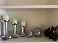 Full lot showing three candlesticks with candles, two silver pig sculptures and two black rabbit figurines arranged on shelf