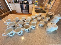 Full set on countertop showing cups, saucers stack, teapot, coffee pot