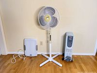 Pedestal fan, radiator heater, and light therapy lamp side by side on floor