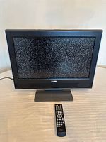 Front view of TV powered on displaying static with remote in foreground