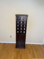 Full front view of tall narrow dark wood cabinet with grid of 15 drawers and lower door