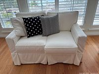 Front view of white slipcovered loveseat with two pillows