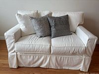 Front view of white slipcovered loveseat with three decorative pillows