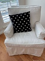 Front view of white slipcovered armchair with black polka-dot cushion