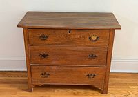 Front view of closed three-drawer ash chest showing brass pulls