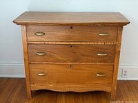 Front view of pine dresser showing three drawers, brass pulls, keyholes and curved skirt