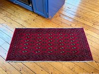Full view of Afghan Bukhara rug on wooden floor showing entire pattern and size