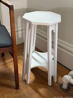 Full view of painted white pine plant stand beside chair