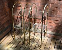 Full view of both brass-tone metal étagères showing arched frames and glass shelves