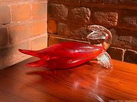 Side view of entire red glass fish sculpture on wood surface