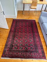 Full view of Afghan rug on wooden floor showing overall design and condition