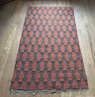 Full view of rectangular Moroccan Berber wool runner showing red and black checkerboard pattern and fringe end
