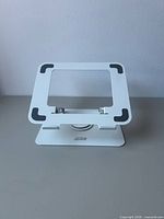 Front view of white metal iCAN stand showing platform with silicone corner grips and rotating base