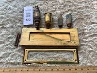 Group shot of all brass hardware including mail slot plates, valve, filter, reservoir, screws with ruler for scale