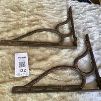 Pair of cast iron ornate brackets laying flat, tag shows lot number and dimensions