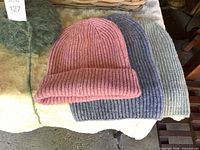 three knit beanies in pink, blue, green on surface