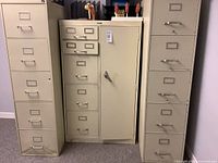 Front view of three beige steel cabinets: two tall five-drawer vertical files flanking a shorter cabinet with drawers and safe door