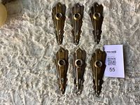 Six brass-plated keyhole backplates front view on fabric surface