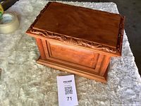 Angled top and side view of cherry wood urn showing carved trim and paneled construction