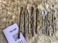 Nine spade drill bits laid out beside lot card