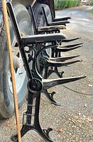 Side view of three cast iron bench ends showing ornate legs and wood armrests