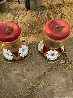 Two red-top hummingbird feeders side by side on ground