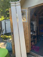 Full length view of both white fluted pillars leaning against shed