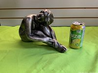 Front three-quarter view of metal seated female nude statue next to can for scale