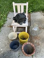 Overview: chair with frog ornament on seat, four planters and glass jug on ground
