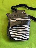 Front view showing zebra-pattern flap, black faux leather body, attached strap