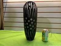 Full view of tall black glass vase beside soda can for scale