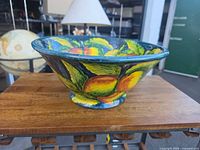 Side view of hand-painted terracotta bowl showing fruit motif and footed base