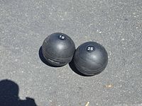 Two black Rep Fitness slam balls showing 10 and 25 weight markings on asphalt