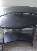 Overall view of black corner desk showing top surface, metal frame, lower shelf