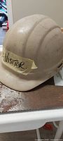 Beige hard hat labelled Visitor resting on saw blade