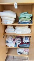 Cabinet shelves filled with folded towels in three stacks, showing range of colours and sizes