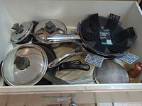 Overview of cookware in drawer showing saucepans with lids, frying pans, protectors