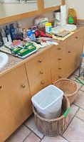 Overall lot on vanity showing toiletries, hair dryer, baskets, waste bin