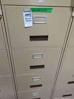 Front view showing multiple beige metal filing cabinets, focus on four-drawer unit with label frames and handles
