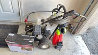 Overall view of pressure washer with hose, spray gun, gas can, oil bottle and boxed accessory