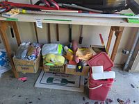 Overview of lot under workbench showing boxes of cloths, yellow towels, sponges, poles and red bucket