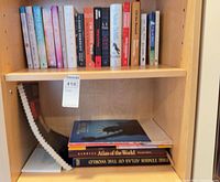Shelf with top row of assorted books and lower row with atlases and spiral booklet