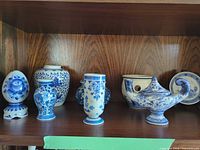 Front view showing six of seven Delft-style porcelain pieces on shelf