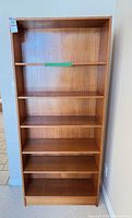 Front view of tall warm-brown veneer bookcase with six shelf levels