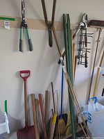 Overview of assorted garden tools including loppers, post-hole digger, stakes, red scoop shovel and broom