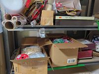 Shelved lot showing rolls of wrap, bags, boxes and two open cartons of bows and ribbon