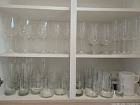Cabinet shelves with full assortment of wine glasses, flutes, tumblers, tall glasses, mugs, shot glass