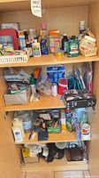 Full cabinet view showing three shelves of mixed toiletries, first-aid, cleaning and miscellaneous items