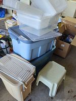 Stack of clear containers on blue totes, step stool and trash bin visible